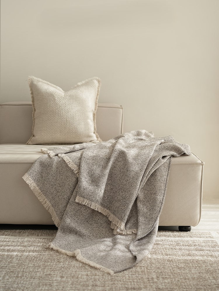 Classic luxe plaid op een beige bank met een bijpassend kussen, gemaakt van wol en premium vezels, met franjes voor een verfijnde uitstraling.