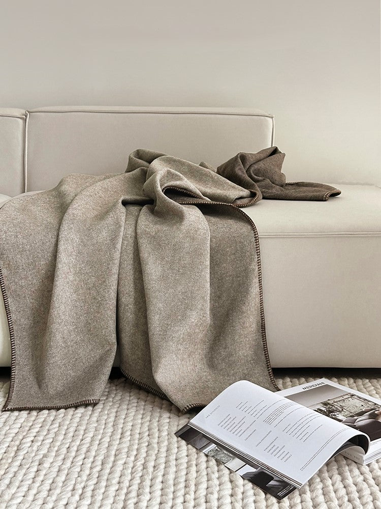 Two-tone deken in beige op een bank met een tijdschrift ernaast, met een elegant geweven ontwerp en een moderne uitstraling.