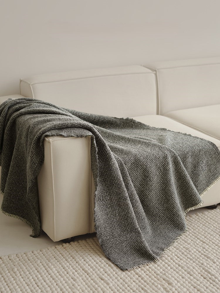 Grijze angora wol en wollen plaid met franjes, gedrapeerd over de hoek van een lichte bank in een moderne woonkamer.