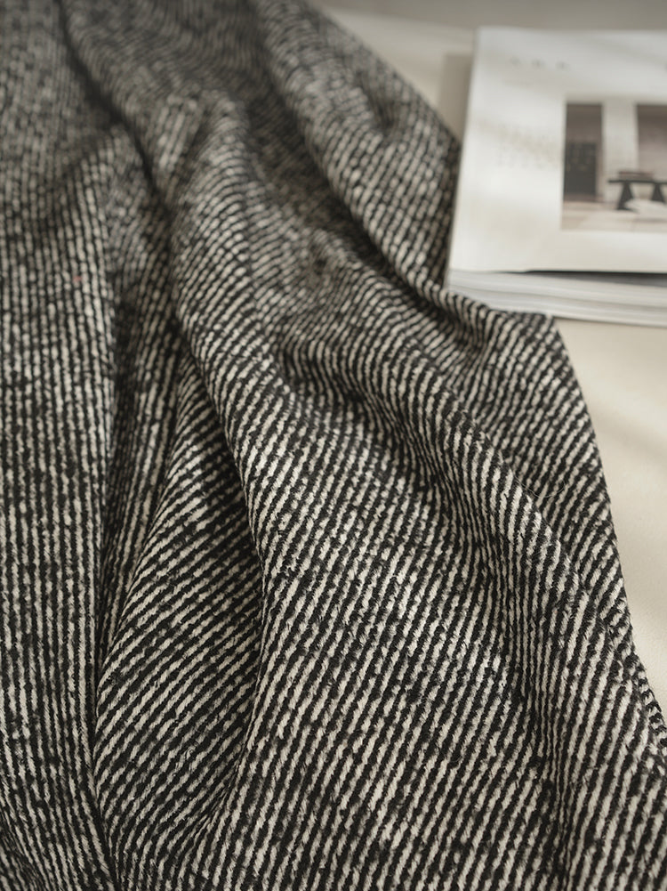 Close-up van een zwarte plaid met een gestreept patroon, liggend op een bank, met een boek ernaast.