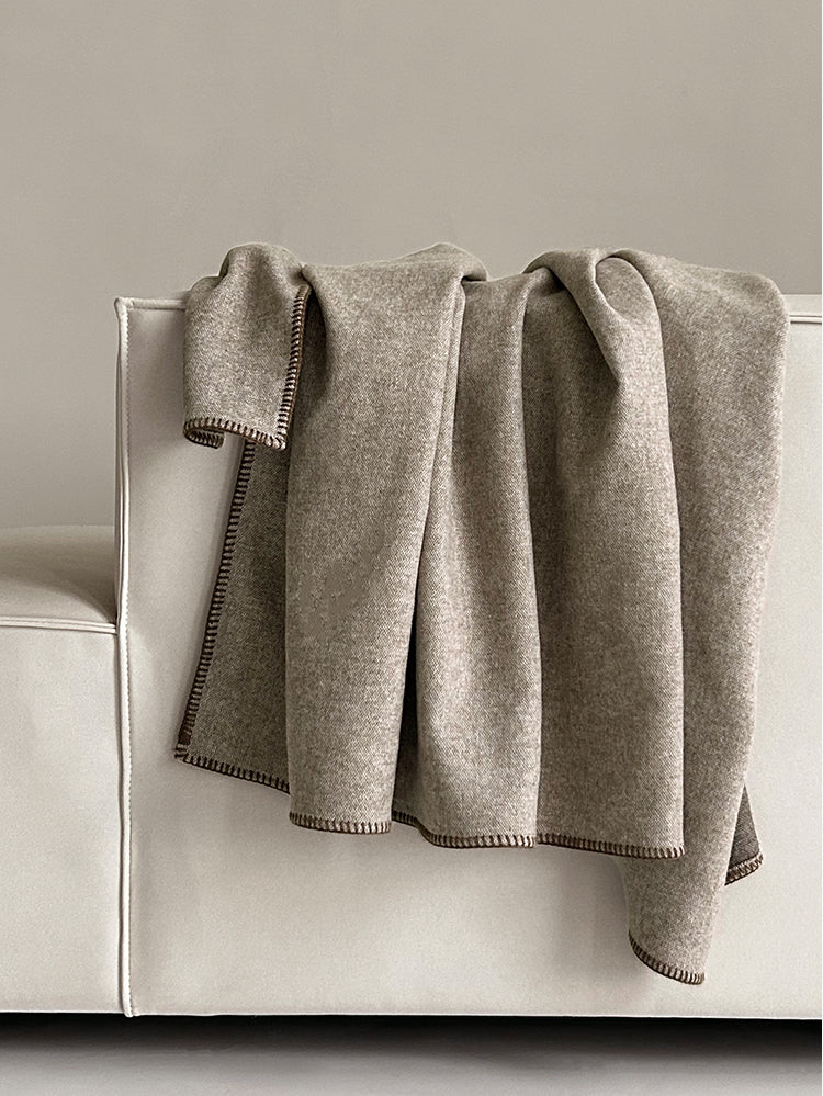 Two-tone deken in warme beige tinten, elegant gedrapeerd over een bank, met een nette, stevige randafwerking in een contrasterende kleur.