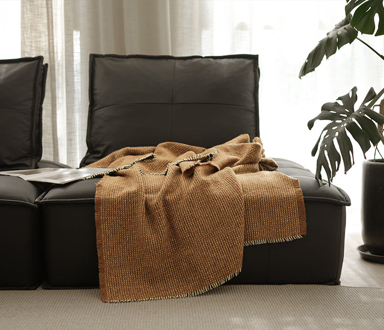 Luxe angora wol en wollen plaid in bruine kleur, met franjes, draperend over een zwarte bank in een stijlvolle woonkamer met planten.