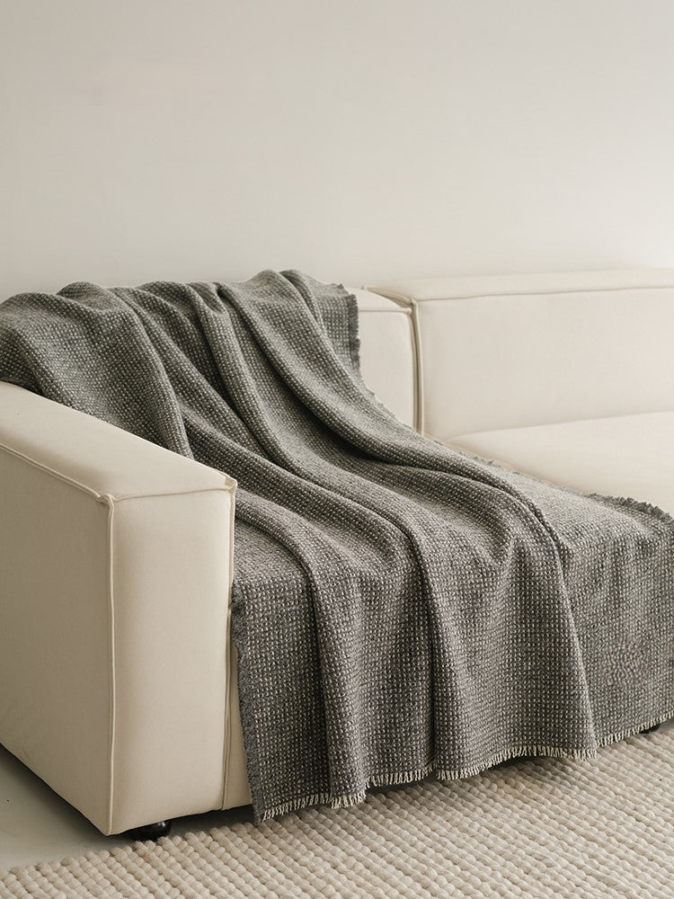 Grijze angora-wol en wollen plaid, met franjes, mooi gedrapeerd over de armleuning van een minimalistische witte bank.