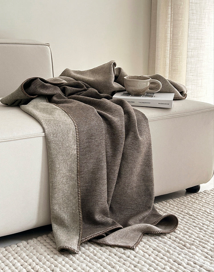 Two-tone plaid in bruin en beige, elegant gedrapeerd over een bank, met een kopje koffie en een boek ernaast voor een gezellige uitstraling.