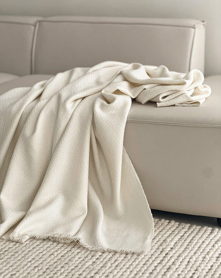 Classic witte Herringbone plaid met franjes die elegant over een bank ligt, gemaakt van luxe wolmix met visgraatpatroon.