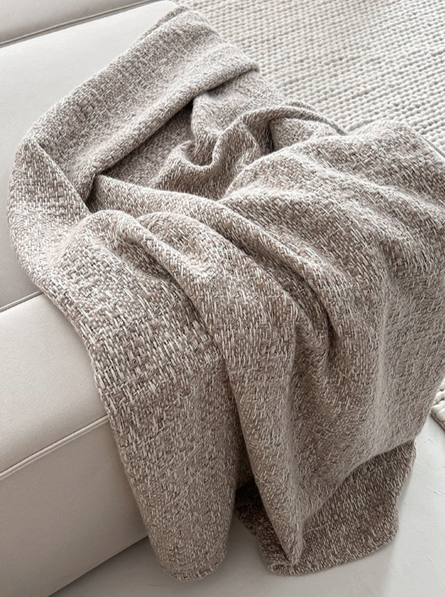 NOLA alpaca wollen plaid in camelkleur, stijlvol gedrapeerd over de rand van een lichtbeige bank, met zicht op een geweven vloerkleed