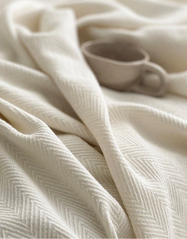 Detail van een luxe Herringbone plaid in wit met visgraatpatroon, met een rustieke keramische kop in de achtergrond.