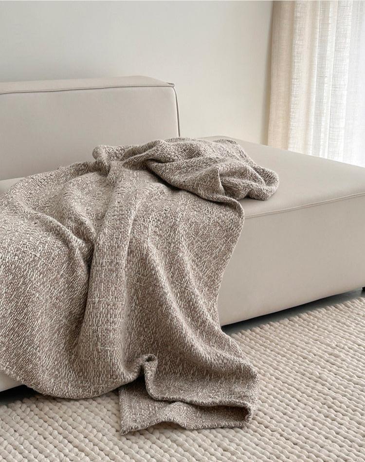 Beige alpaca wollen plaid op een lichtbeige bank, met natuurlijke lichtinval en een geweven vloerkleed