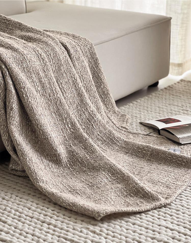 NOLA alpaca wollen plaid in camelkleur, gedrapeerd over een lichtbeige bank en vloeiend over een geweven vloerkleed in een warme, rustige setting