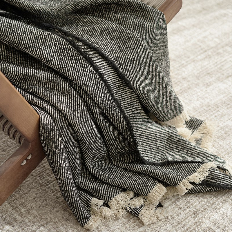 De zwarte plaid over een stoel gedrapeerd, met zachte franjes, die de premium wol en textuur laat zien