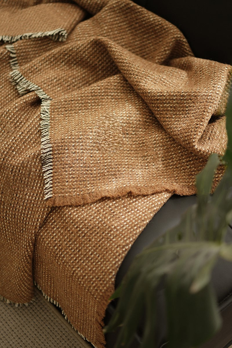 Close-up van een bruine angora wol en wollen plaid met franjes, liggend op een zwarte bank in een stijlvolle woonkamer.