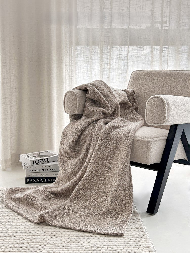 NOLA alpaca wollen plaid in camelkleur gedrapeerd over een beige bouclé fauteuil, met designboeken en een geweven vloerkleed in een lichte ruimte