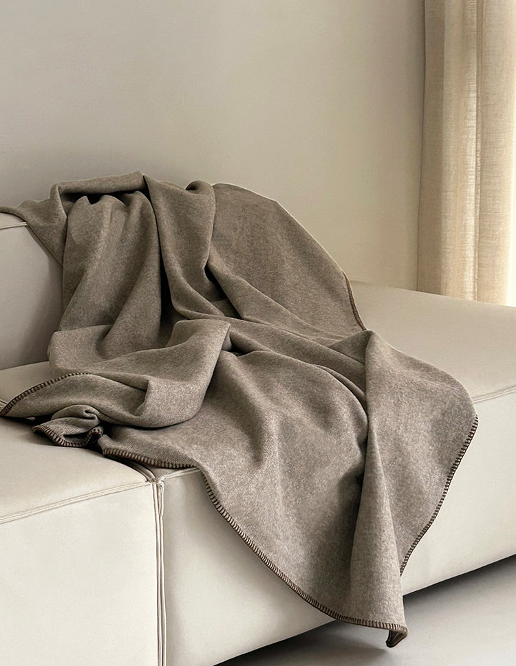 Two-tone deken in warme beige kleur, rustig over de bank gedrapeerd, met een elegante randafwerking.