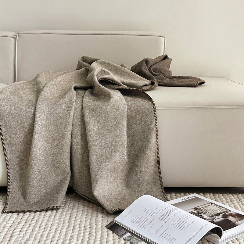 Two-tone deken in beige en bruin op een bank met een tijdschrift ernaast, met een elegant geweven ontwerp en moderne uitstraling.
